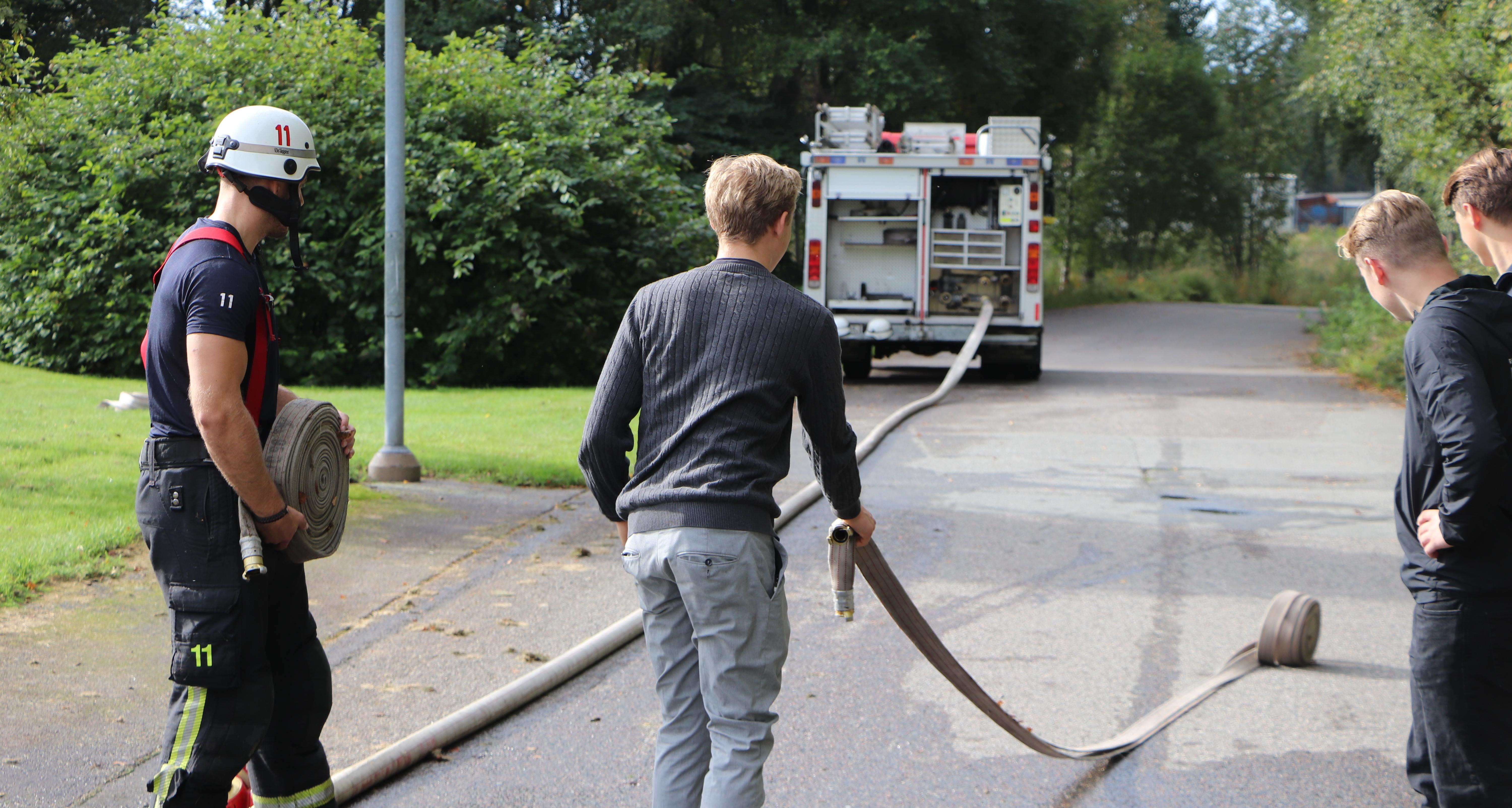 En person från räddningstjänsten visar ungdomar hur man använder en brandslang.